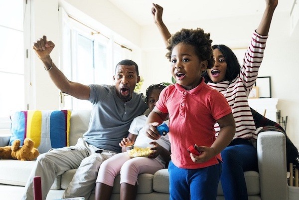 scene of love; two parents and two children sitting on a couch; they are excited, cheering with their hands in the air