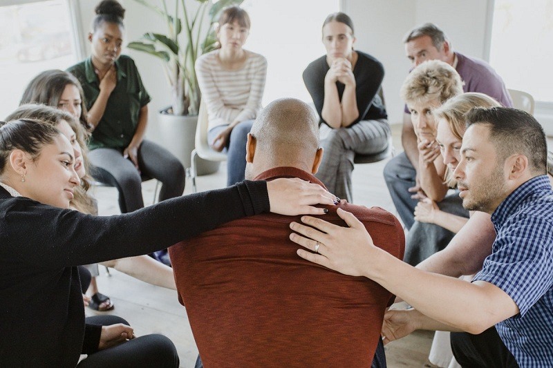 a support group as part of a group session, hands on the back of a man who is sharing in a circle