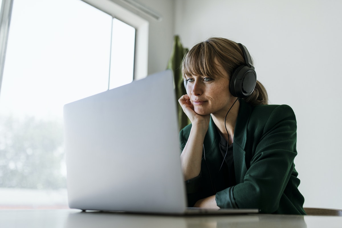 woman with headphones on smiling and looking at laptop