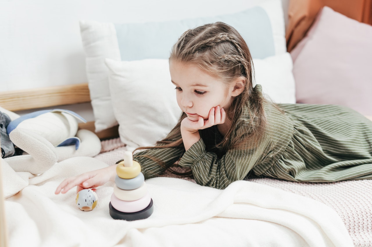 A young girl living with ADHD plays with wooden toys on her bed.