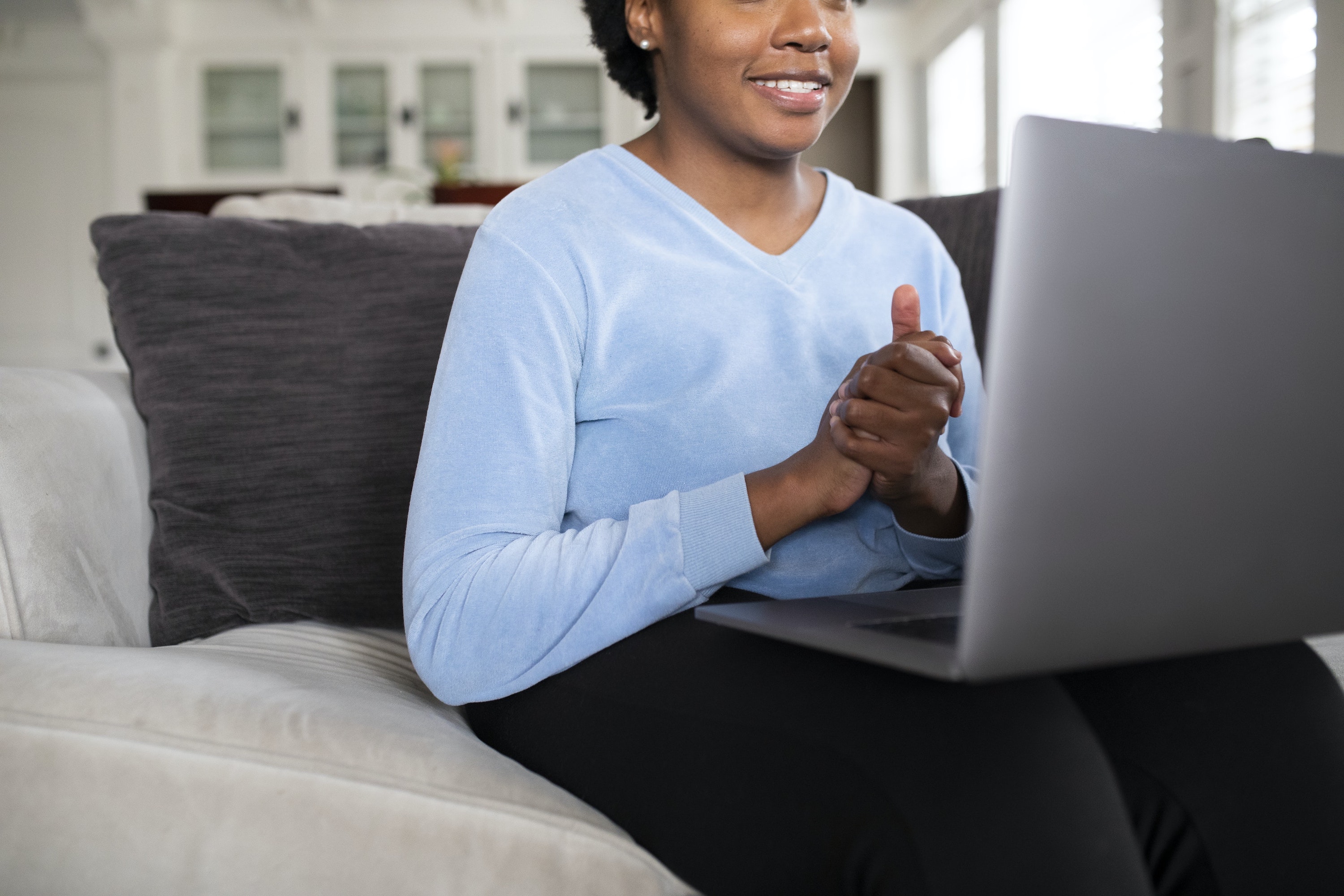 women clasping hands together and smiling while looking at computer screen in her living room