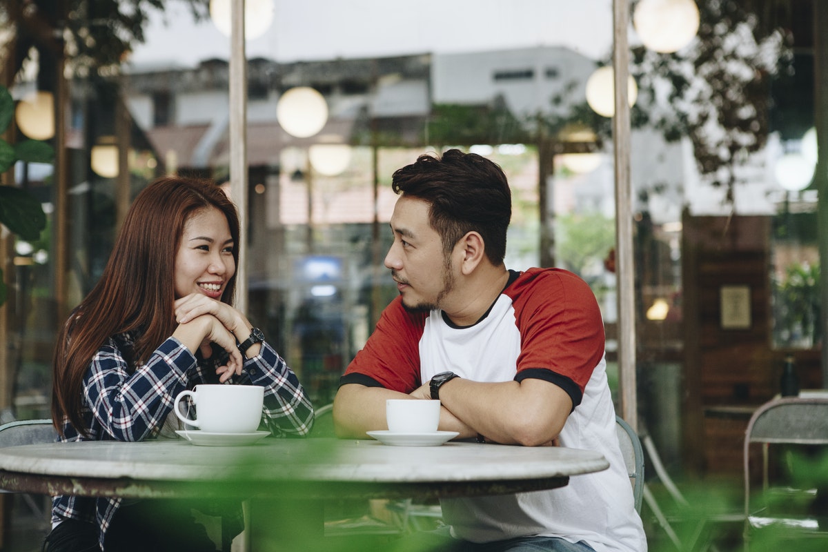 man and woman sitting at a cafe table drinking coffee and having a conversation